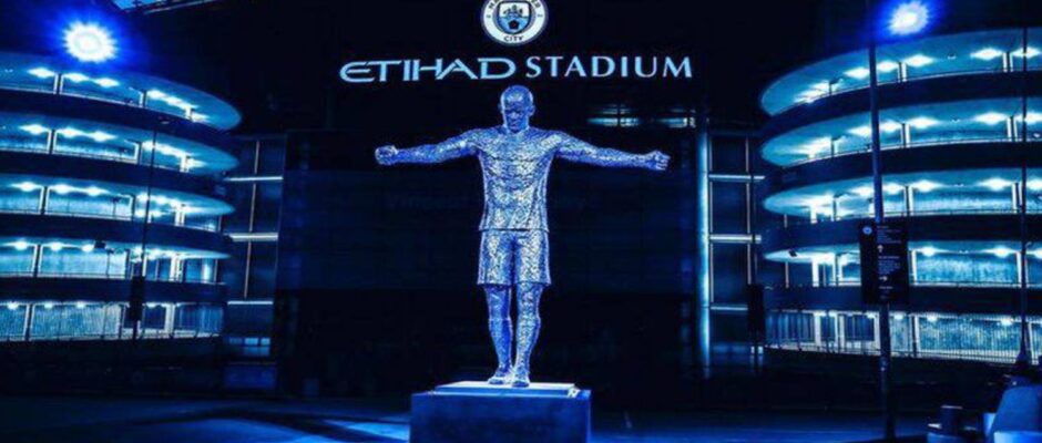 Entrada del estadio Etihad con estatua de jugador de brazos abiertos al frente